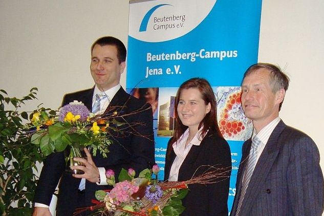 zwei Männer einer mit Blumenstrauß und eine Frau mit Blumenstrauß in der Mitte